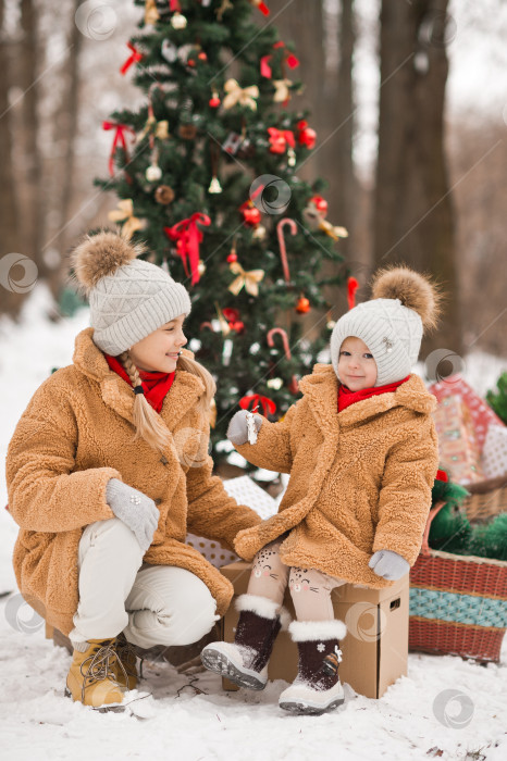 Скачать Дети играют с подарками рядом с украшенной рождественской елкой в зимний снежный день. фотосток Ozero