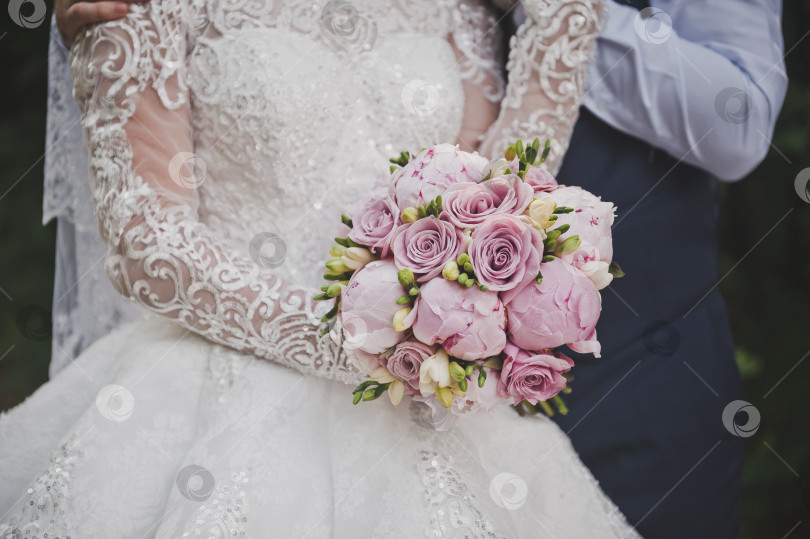 Скачать Невеста стоит рядом с женихом и держит в руках яркий свадебный букет из пионов и роз 2667. фотосток Ozero