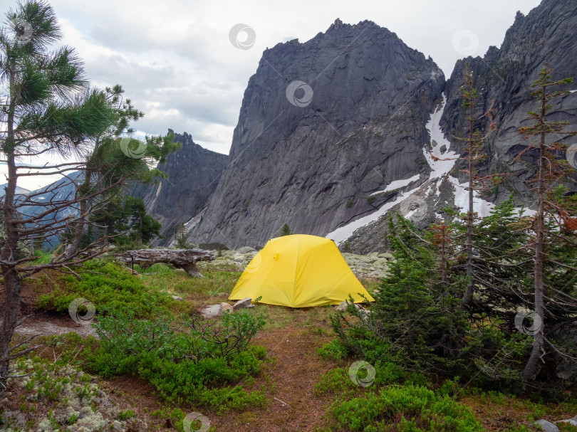 Скачать Драматический пейзаж с желтой палаткой на лесном холме среди скал фотосток Ozero