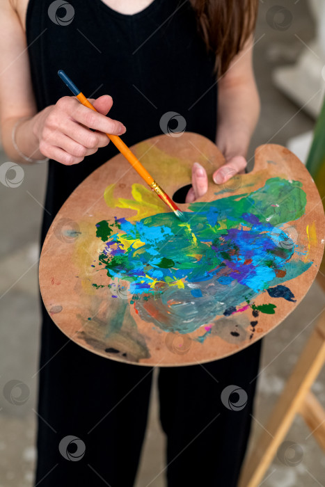 Скачать Художник художник стоит в студии, держа в руках кисть и палитру со смешанными красками фотосток Ozero