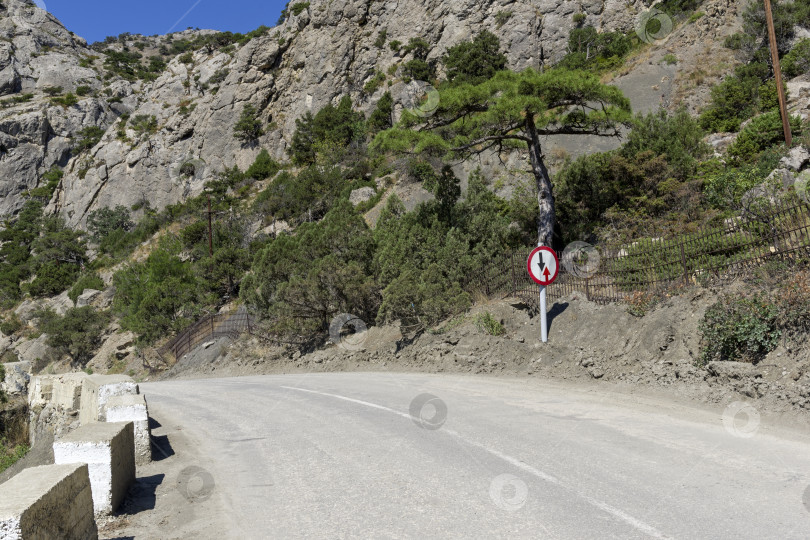 Скачать Дорожный знак "Уступите дорогу встречному движению" на опасном повороте на горной дороге. фотосток Ozero