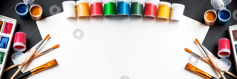 Скачать Художественный баннер с разноцветными банками гуашевых красок, кистями и бумагой для рисования на столе фотосток Ozero