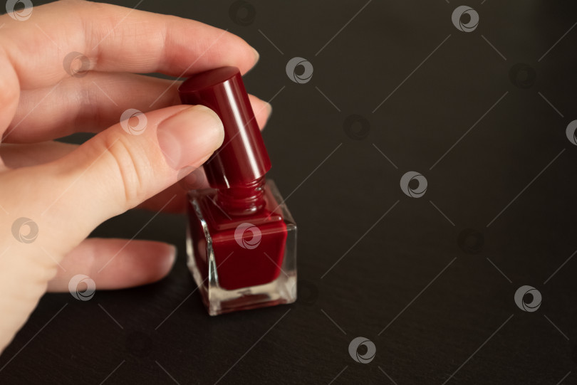Скачать Женская рука с наманикюренными ногтями открывает маленький флакончик с красным лаком для ногтей фотосток Ozero