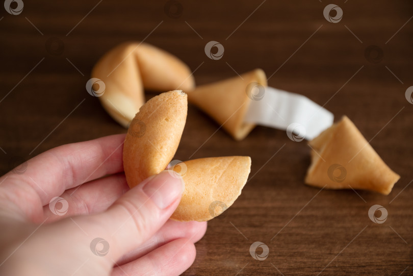 Скачать Человек, держащий в руке печенье с предсказанием судьбы на фоне нескольких печений, лежащих на поверхности стола фотосток Ozero