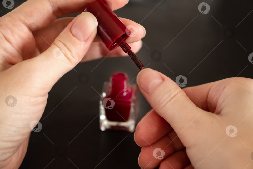Скачать Крупным планом руки женщины, готовой нанести красный лак на ногти, процедура маникюра в домашних условиях фотосток Ozero