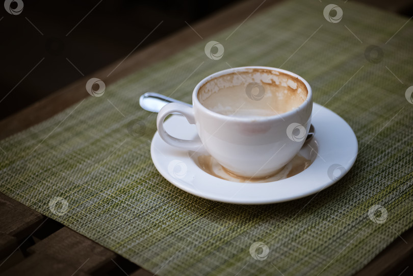 Скачать Пустая кофейная чашка с пятнами молочной пены по краям, оставленная на столике уличного кафе фотосток Ozero