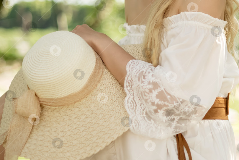 Скачать Женщина в белом платье сидит, положив руку на колено и держа соломенную шляпу, летний образ жизни на свежем воздухе фотосток Ozero
