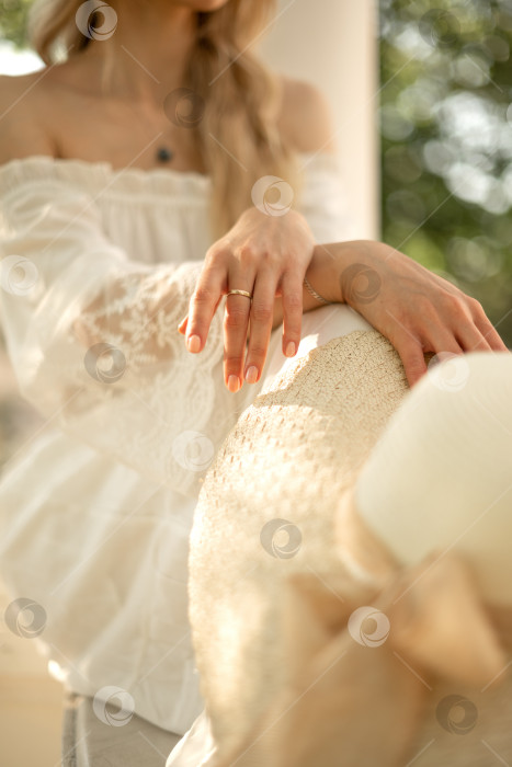 Скачать Молодая женщина сидит, скрестив руки на колене и держа в руках соломенную шляпу, летний образ жизни на свежем воздухе фотосток Ozero