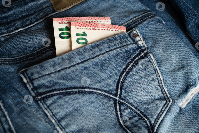 Скачать Две банкноты по десять евро выглядывают из заднего кармана старых синих джинсов фотосток Ozero