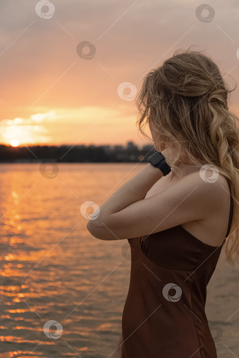 Скачать Молодая женщина любуется закатом на берегу реки летним вечером фотосток Ozero