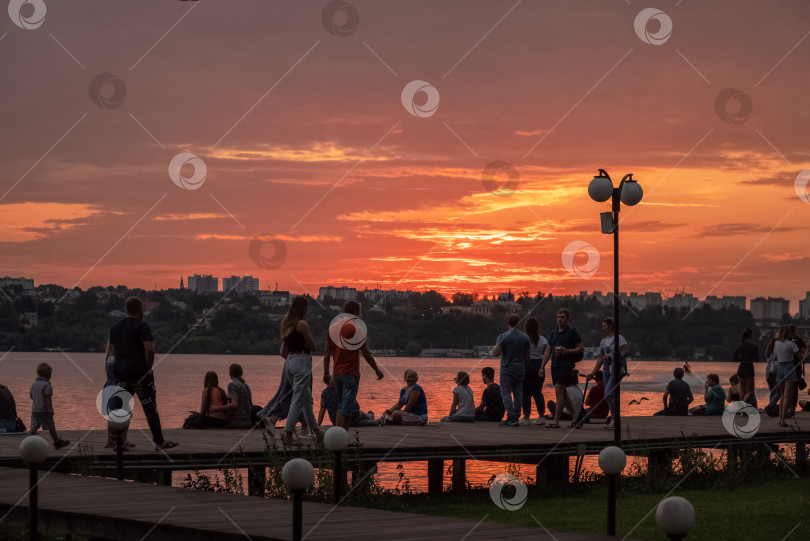 Скачать летним вечером люди любуются закатом на набережной фотосток Ozero