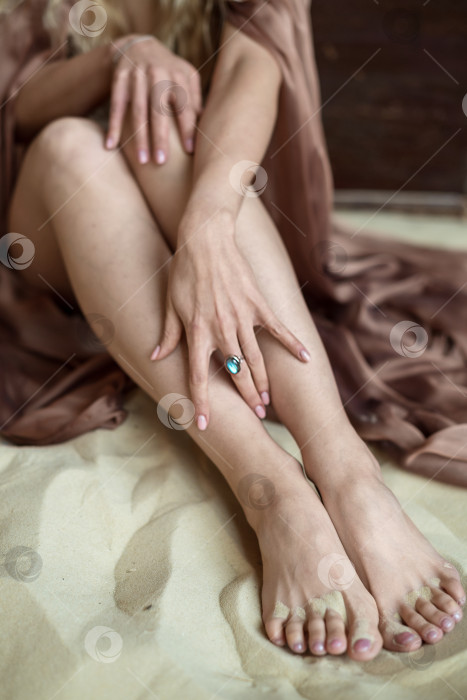 Скачать женщина сидит на песке, касаясь рукой своих ног с винтажным кольцом на пальце фотосток Ozero