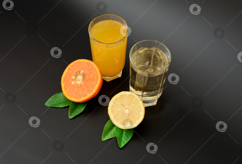 Скачать Два бокала с разными цитрусовыми соками на черном фоне, рядом с половинкой спелого лимона и апельсином с листьями. фотосток Ozero