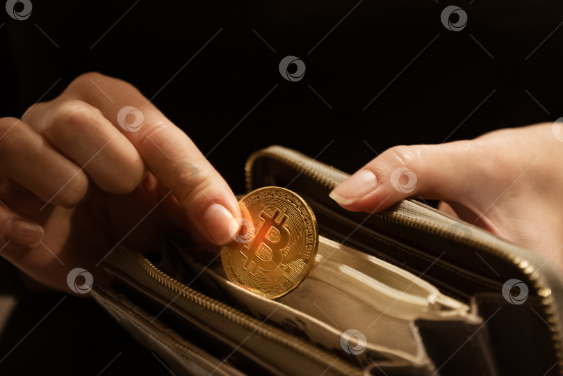 Скачать Женщина кладет золотую биткойн-монету в свою сумочку, крупным планом сняты руки фотосток Ozero