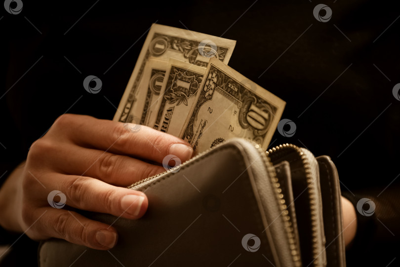 Скачать Женщина кладет долларовые банкноты в кошелек или вынимает их из него на темном фоне фотосток Ozero