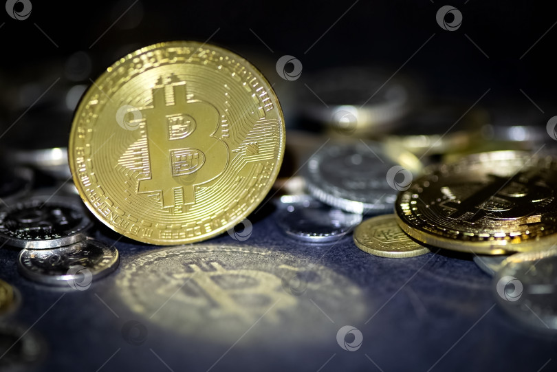 Скачать Золотая криптовалюта биткоин отражается светом на темной поверхности, металлические монеты рассыпаются на заднем плане. фотосток Ozero