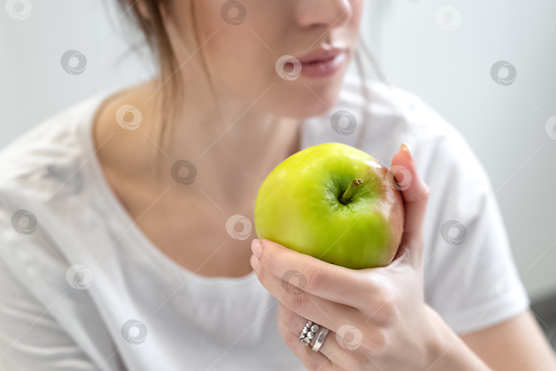Скачать Молодая женщина в белой футболке держит в руке зеленое спелое яблоко. Диета и здоровое питание фотосток Ozero