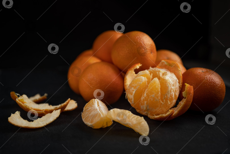 Скачать Очищенные ломтики и половинка мандарина на темной поверхности стола фотосток Ozero