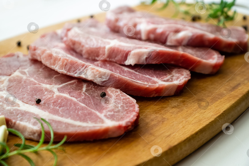 Скачать Нарезанное ломтиками сырое свиное мясо со свежим розмарином и перцем выложите на разделочную доску фотосток Ozero