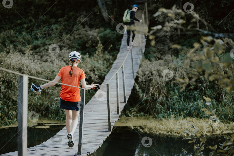 Скачать Вид сзади на молодую женщину, пересекающую реку по деревянному подвесному мосту фотосток Ozero