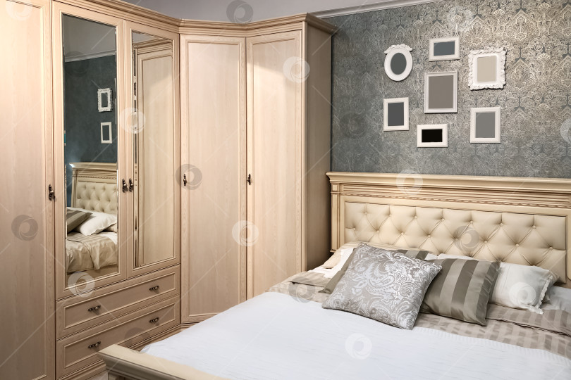 Скачать Классический интерьер спальни с мебелью из натурального дерева и удобной двуспальной кроватью с подушками и фоторамками на стене фотосток Ozero
