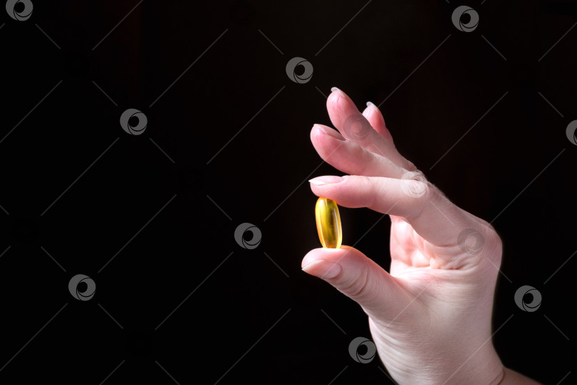 Скачать Человеческая рука в жесте "ок" держит золотую таблетку. Темный фон фотосток Ozero