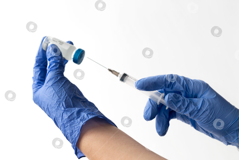 Скачать Крупный план рук в синих медицинских перчатках, держащих шприц и флакон с вакциной на светлом фоне. Профилактическая вакцинация против COVID-19, концепция коронавируса фотосток Ozero