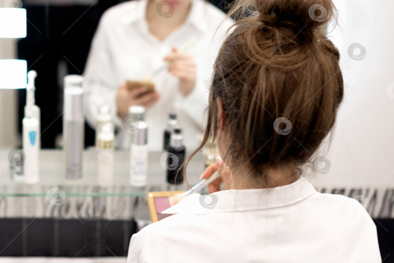 Скачать Молодая женщина делает макияж, стоя перед зеркалом в ванной фотосток Ozero