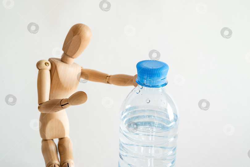 Скачать Деревянный манекен держит пластиковую бутылку с водой. Питьевая вода, здоровый образ жизни фотосток Ozero