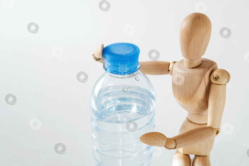 Скачать Крупным планом деревянный манекен держит пластиковую бутылку с водой. Питьевая вода, здоровый образ жизни фотосток Ozero