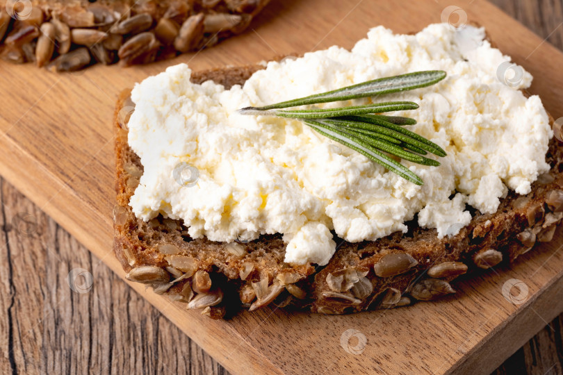 Скачать Домашний хлеб на деревянной разделочной доске с творожным сыром, рикоттой и розмарином. фотосток Ozero