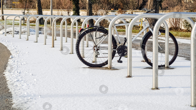 Скачать Велосипед припаркован на пустой уличной велопарковке, припорошенной первым снегом фотосток Ozero