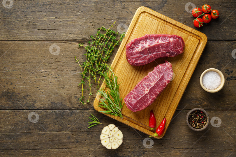 Скачать Вкусный говяжий стейк с двумя сырыми верхними лезвиями на деревянной доске со специями и зеленью фотосток Ozero