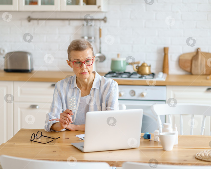 Скачать Пожилая женщина разговаривает онлайн с врачом о лекарствах, лечении, сидя дома на кухне фотосток Ozero
