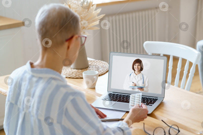 Скачать Безликая пожилая женщина разговаривает онлайн с врачом, сидя дома на кухне фотосток Ozero