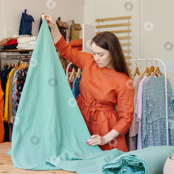 Скачать Женщина-модельер измеряет ткань во время работы в швейной мастерской фотосток Ozero