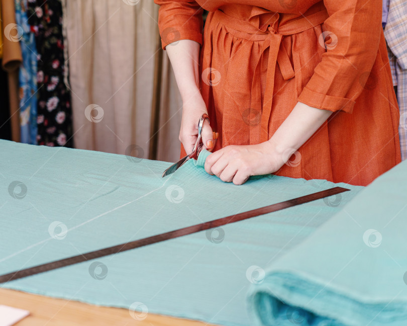 Скачать Женщина-модельер или портной, разрезающая ткань на столе перед пошивом одежды в ателье фотосток Ozero