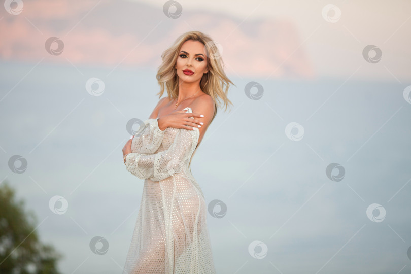 Скачать девушка в прозрачном белом платье стоит на скале и смотрит на море. фотосток Ozero