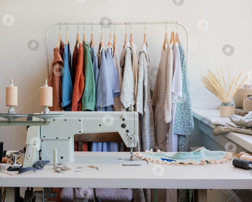 Скачать Интерьер модного ателье с профессиональной швейной машинкой и коллекцией модных платьев на вешалках фотосток Ozero