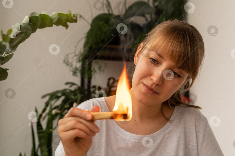 Скачать Молодая женщина смотрит, как горит ароматическая деревянная палочка. Практика ароматерапии благовониями фотосток Ozero