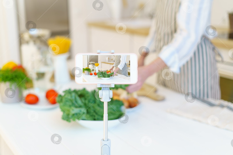 Скачать Женщина-блогер записывает видео-рецепт на телефон для блога во время приготовления пищи на кухне дома фотосток Ozero