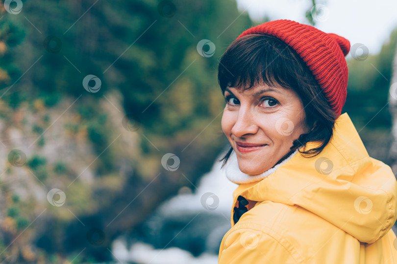 Скачать Наедине с природой. Вид сзади улыбающейся женщины, смотрящей в камеру возле водопада, фотосток Ozero