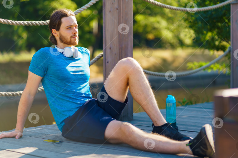 Скачать Молодой раскованный спортивный мужчина отдыхает после утренней тренировки на природе фотосток Ozero
