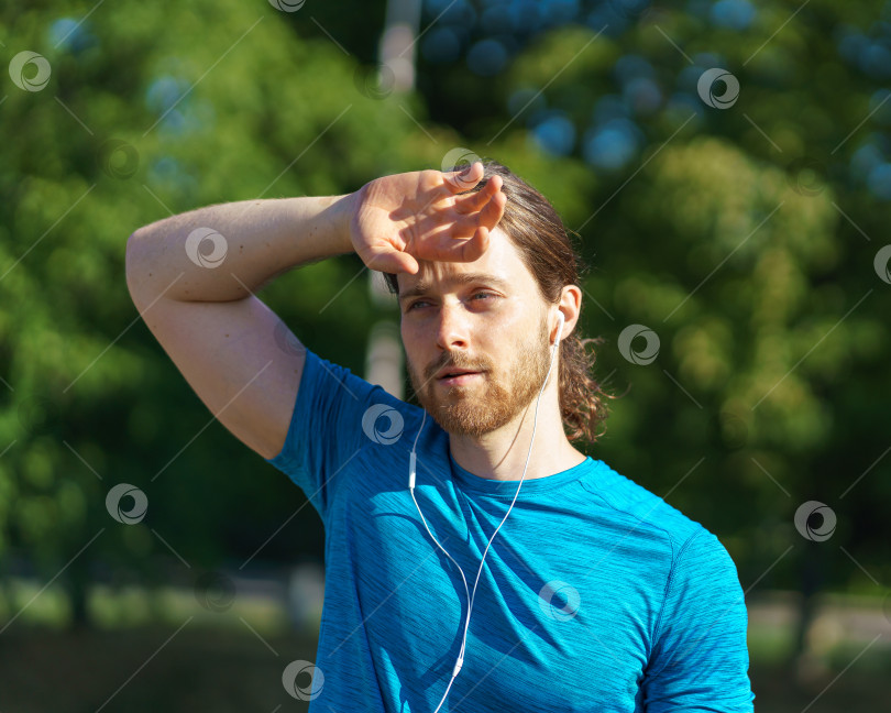 Скачать Усталый измученный молодой спортивный мужчина вытирает пот со лба во время тренировки на открытом воздухе фотосток Ozero