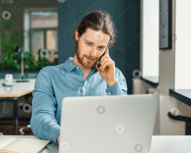Скачать Молодой занятой мужчина-предприниматель разговаривает по мобильному телефону в офисе фотосток Ozero