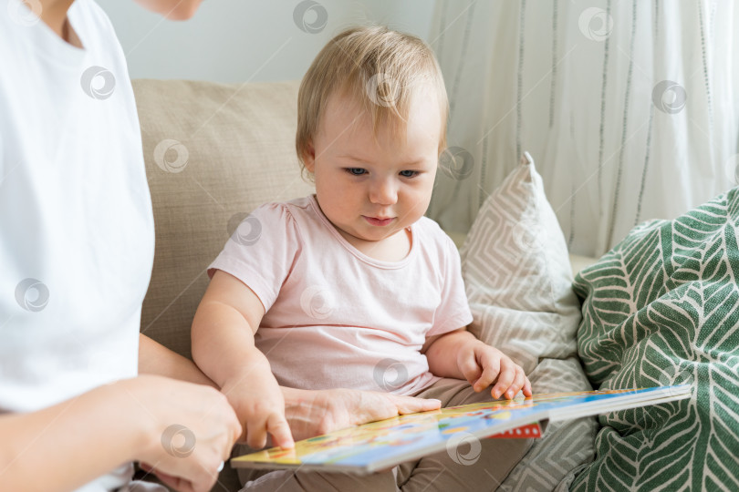 Скачать Крупным планом портрет безликой женщины, читающей книгу с серьезным ребенком на диване. Естественное освещение фотосток Ozero