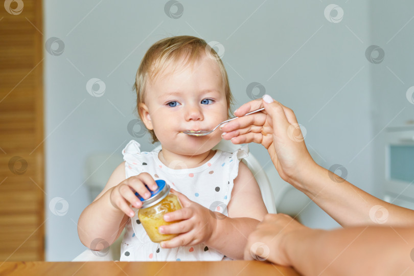 Скачать Ребенок сидит на высоком стульчике, пока мама кормит малыша дома фотосток Ozero