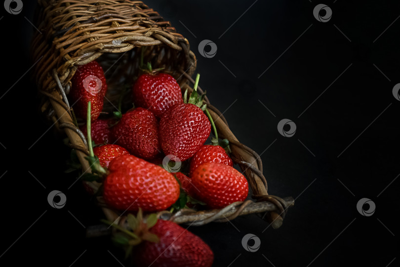 Скачать Плетеная корзина лежит на темной поверхности, полная красной спелой клубники, на фоне летней еды фотосток Ozero