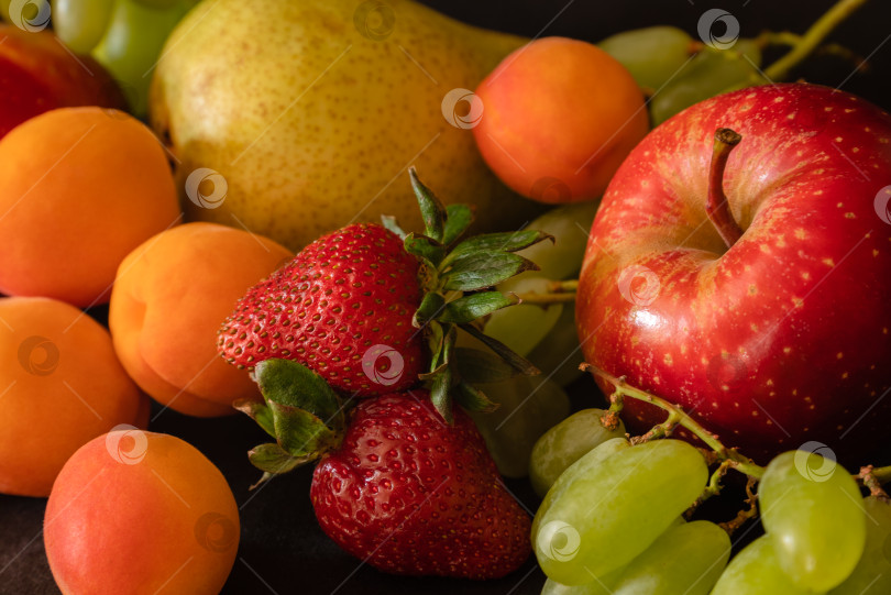 Скачать Фруктовый ассортимент из свежих фруктов - виноград, клубника, абрикосы, груша, яблоко - на черном фоне фотосток Ozero