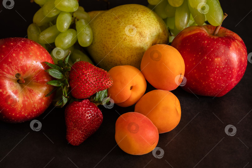 Скачать Фруктовый ассортимент из свежих фруктов - виноград, клубника, абрикосы, груша, яблоко - на черном фоне фотосток Ozero